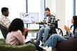 © sofiko14 - Multiracial team including young adult man in wheelchair collaborating on business presentation, discussing economic trends in open workspace. Evening meeting showcasing teamwork, inclusion