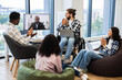 © sofiko14 - Diverse group of colleagues including man in wheelchair and a woman engaging in virtual meeting with African male speaker on screen, demonstrating teamwork, inclusivity, online collaboration.