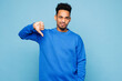 © ViDi Studio - Young sad man of African American ethnicity wears sweatshirt casual clothes showing thumb down dislike gesture isolated on plain pastel light blue cyan background studio portrait. Lifestyle concept.
