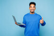 © ViDi Studio - Young IT man of African American ethnicity wears sweatshirt casual clothes hold use work on laptop pc computer show thumb up isolated on plain pastel light blue background studio. Lifestyle concept.