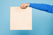 © ViDi Studio - Close up cropped male holding brown clear blank craft paper takeaway bag mock up isolated on pastel plain light blue wall background studio. Courier delivery concept. Copy space advertising mock up.