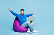 © ViDi Studio - Full body winner young IT man wear sweatshirt casual clothes sit in bag chair hold use work on laptop pc computer isolated on plain pastel light blue cyan background studio portrait Lifestyle concept