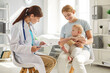 © Studio Romantic - Mother and child visit pediatrician at clinic. Happy young woman holding her cute little baby on her lap while sitting on chair and talking to friendly, smiling doctor. Children's healthcare concept