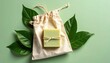 © Ukasyah - A light green bar soap rests in an off-white drawstring bag, surrounded by vibrant green leaves on a pale green background.  The image is styled for a minimalist, natural product feel