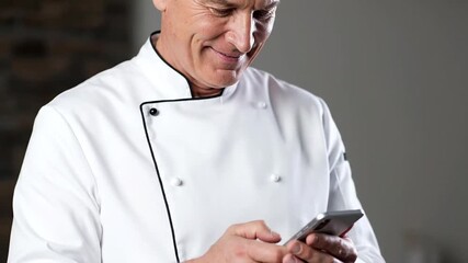 Chef in uniform uses a smartphone indoors with neutral background