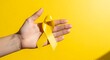 © Ulfiatul Savira - Human Hand Holding a Yellow Awareness Ribbon on Vibrant Yellow