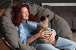 © Tatyana Gladskih - Cheerful Young Woman sitting on Couch with Dog at home