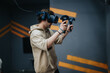 © qunica.com - A young man immersed in a virtual reality gaming environment, using head-mounted gear and hand held controllers. Set in a contemporary indoor space, emphasizing interactive entertainment.