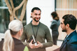 © Maskot - Smiling young male business professional talking with coworkers while at networking event standing in convention center