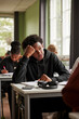 © Maskot - Thoughtful teenage boy leaning on elbows while looking away sitting in classroom at school