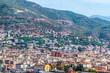 View of the Alanya hillside in Turkey with the I Love Alanya sign visible, surrounded by residential buildings. The background showcases the green mountains and the urban landscape of the Turkish city
