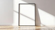 © Tufayel - Black frame mockup leaning against white wall with sunlight shining through the window, creating a bright and inviting atmosphere, perfect for showcasing artwork or photography in a minimalist style