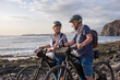 © luciano - Senior active couple riding on the pebble beach with electric bicycles at sunset. Authentic elderly retired life and sustainable mobility concept