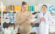 © JackF - Focused pregnant woman scanning QR code on package of medicine with smartphone, checking potential side effects while pharmacist waiting to assist with professional advice standing in background..