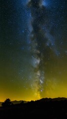 Wall Mural - Dramatic night sky with a vast, bright Milky Way galaxy over silhouetted mountains and trees in a serene rural landscape.