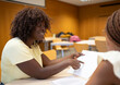 © VictorCanalesStudio - African american teacher students collaborating on academic paperwork in a classroom