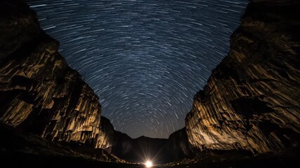 Wall Mural - Star trails arc gracefully across a dark night sky viewed from a majestic cave entrance timelapse astrophotography, discovery, timelapse