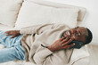 © SHOTPRIME STUDIO - Smiling African man talking on the phone while relaxing on a couch, wearing a cozy sweater and jeans, showcasing a warm and inviting atmosphere