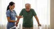 © Kartono - A healthcare professional assists an elderly man with physical therapy, supporting his arm as he walks.