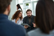 © pressmaster - Confident bearded businessman explaining new company strategies, holding tablet and gesticulating. His curly coworker sitting next to him and looking at plan on his tablet screen attentively