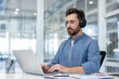 © Liubomir - Focused man wearing headphones working on laptop in modern office