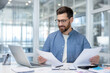 © Liubomir - Businessman reading financial documents at office desk happily
