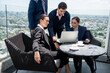 © chachamp - Business team working together on a laptop at outdoor or rooftop office with city background