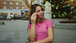 © Krakenimages.com - Woman holding makeup sponge smiling on busy city street in vibrant two-story background, wearing pink shirt with blurred festive lights, expressing happiness outdoors.