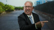© Krakenimages.com - Senior man in a business suit angrily pointing on a street location, capturing a moment of outdoor confrontation with trees and buildings in the background.