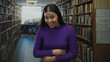 © Krakenimages.com - Woman laughs and holds her stomach amid tall library shelves in a quiet aisle wearing a purple sweater; happiness.