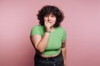 © bodnarphoto - Curly-haired person in a green shirt shows a thoughtful expression against a pink background during an indoor photo session