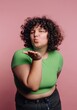© bodnarphoto - Woman blowing a kiss while posing in a bright green top against a pink background