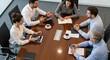 © Alice E - A group of business professionals collaborating on a project at a conference table. They use laptops, tablets, and documents, demonstrating teamwork and productivity in a modern office setting.