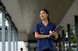 © PaeGAG - Asian doctor woman smiling, holding clipboard in hospital hallway