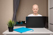 © yta - Oncology survivor at home office desk with laptop, loyal pet dog on bed nearby, online communication and emotional support