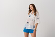 © LIGHTFIELD STUDIOS - Young woman confidently showcases fashionable summer attire in a bright and airy setting