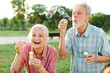 © Lumos sp - Happy active senior couple having fun blowing soap bubbles in park outdoors. Vitality and active senior couple concept