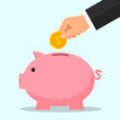 © Nupi Studio - Close-up of a person's hand inserting a coin into a piggy bank, symbolizing saving money and financial planning