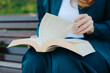 © Anton Pentegov - young woman holds thick book in hands, reading book, sitting on bench in park, close-up view, no face