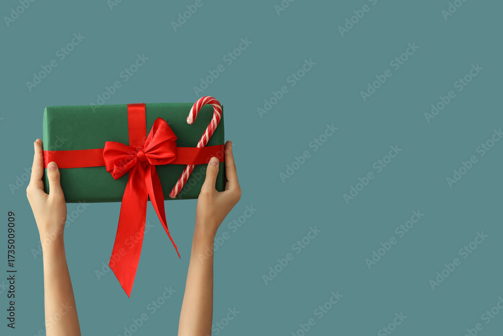 Female hands holding Christmas gift with candy cane on blue background