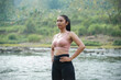 © Nasrul Ma Arif - A slender Asian girl with brown skin in sportswear is doing hip circle stretching movements in the open air on the edge of a beautiful river, before doing sports.