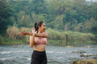 © Nasrul Ma Arif - A slender Asian girl with brown skin in sportswear is doing shoulder muscle stretching movements in the open air on the edge of a beautiful river, before doing sports.