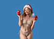© Pixel-Shot - Attractive young woman in swimsuit with Santa hat and Christmas balls on blue background