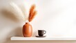 © musthofa - A terracotta vase with pampas grass and a dark coffee cup on a white shelf against a light beige wall presents a simple yet stylish interior design element.