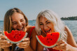© svetograph - Watermelon Beach Summer: Two women joyfully eating watermelon slices on sunny beach.