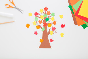 Wall Mural - Created brown tree with colorful maple leaves from application paper on light gray table background. Closeup. Making autumn decoration. Child handcraft. Top down view.
