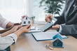© doidam10 - Close up of real estate agent handing house model to client with calculator and contract paperwork on desk, concept of mortgage loan, home ownership, property investment and housing agreement.