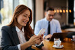 © Drazen - Happy female entrepreneur texting on cell phone during business meeting in cafe.