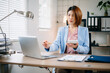 © laddawan - Asian businesswoman using calculator and laptop for financial planning in bright office. Ideal for finance, accounting, tax