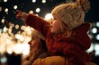 © Yevheniia - Joyful caucasian child on mother's shoulders enjoying festive lights with cheerful wonder